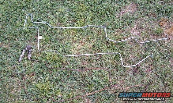 Two sets of metal brake lines on grass, one set is silver and the other is rusted brown