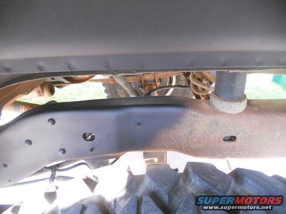 Vehicle frame with rust and black paint, leaf springs, shock absorber, and tire tread visible