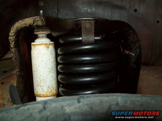 Close-up of a black coil spring and white shock absorber in a vehicle's wheel well