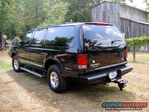 Black 2005 Ford Excursion SUV, rear 3/4 view, parked on grass near a wooden barn