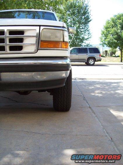 Front corner of a white pickup truck, with a silver SUV in the background