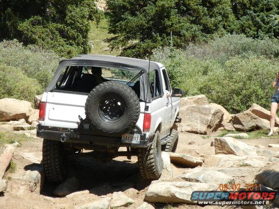 White 1996 Ford Bronco convertible with spare tire on rear, off-roading on rocky terrain