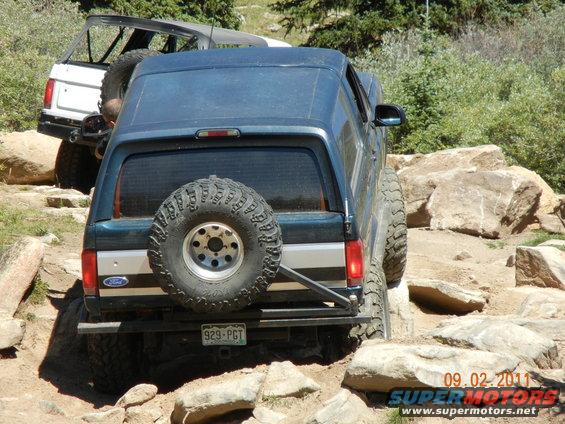 Dark blue Ford Bronco with spare tire on rear, navigating rocky terrain