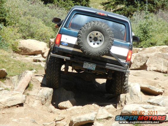 1996 Ford Bronco navigating a rocky trail, rear view with spare tire mounted