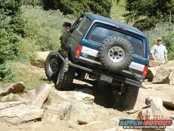 Ford Bronco on a rocky trail, driver's side visible, spare tire on back