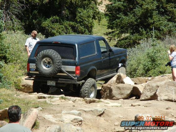 Dark blue 1996 Ford Bronco with spare tire on rear, navigating rocky terrain