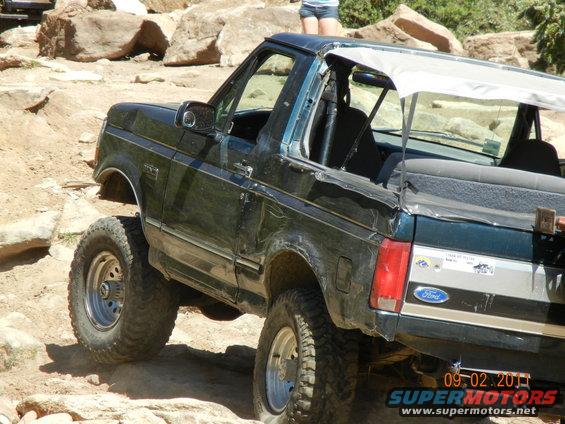 Dark green 1996 Ford Bronco with a soft top, off-roading on rocks