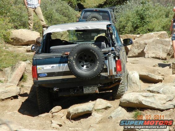 1996 Ford Bronco navigating rocks, spare tire mounted on rear. Another SUV behind