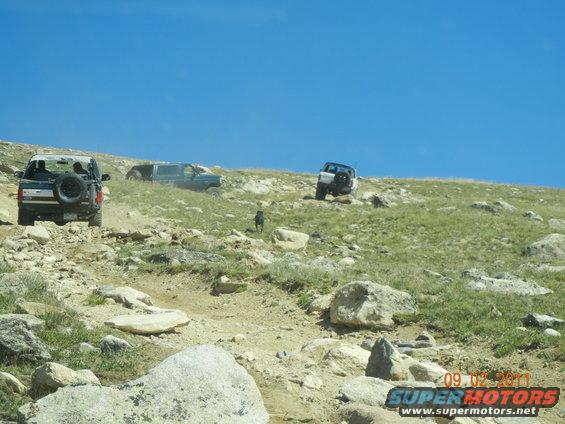 Three SUVs on a rocky hill; one in foreground rear-view, one in mid-ground side-view, one in background rear-view