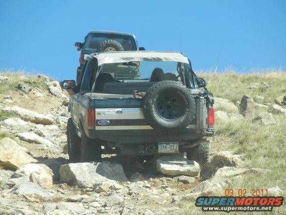 Rear view of a 1996 Ford Bronco on a rocky trail, with a spare tire mounted on the back