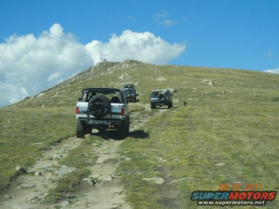 White Ford Bronco with spare tire on rear, driving on a rocky mountain trail