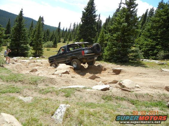 Black Ford Bronco navigating rocky terrain, spare tire mounted on rear