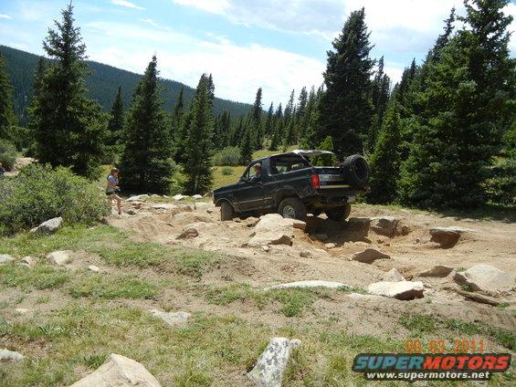 Dark 1996 Ford Bronco on rocky trail, rear-mounted spare tire visible