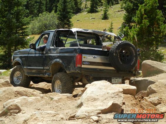 Black Ford Bronco with a soft top, driving over rocks on a dirt trail
