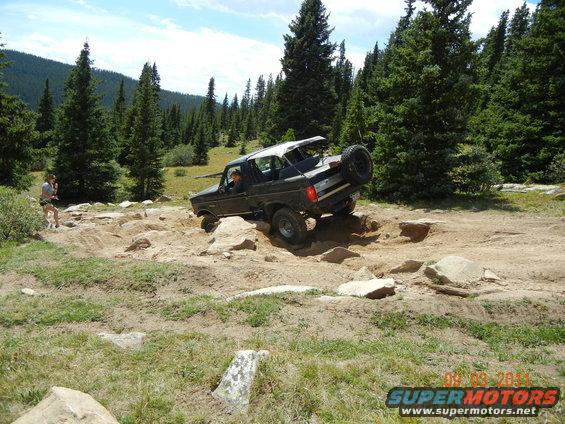 1996 Ford Bronco navigating a steep, rocky off-road trail with a person standing nearby