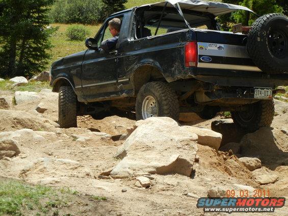 1996 Ford Bronco navigating a rocky trail, driver visible, spare tire mounted on rear
