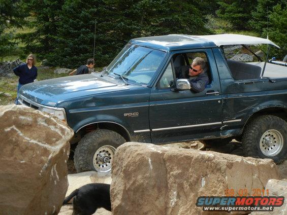 1996 Ford Bronco navigating a rocky off-road trail with people and a dog nearby