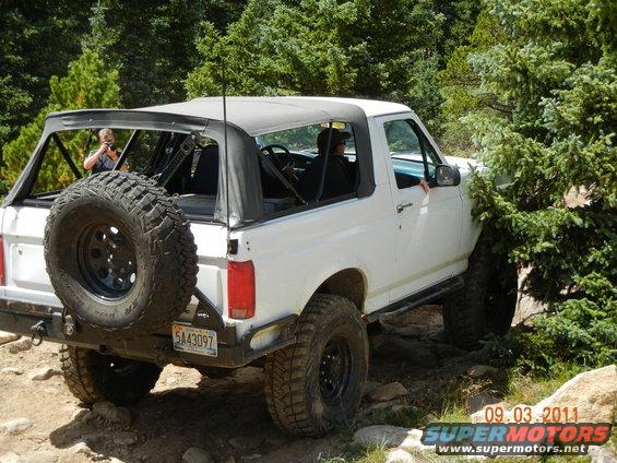 White 1996 Ford Bronco convertible with spare tire on rear, off-roading on rocky terrain