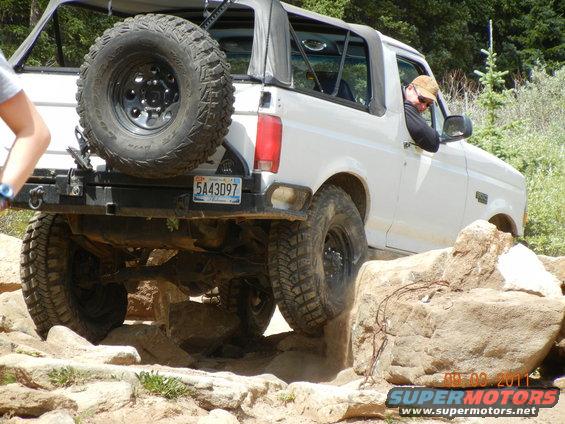 White 1996 Ford Bronco with spare tire on rear bumper, navigating rocky terrain