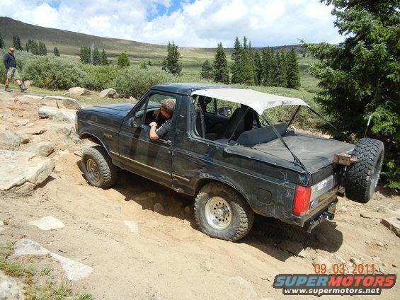 Black 1996 Ford Bronco with soft top on a rocky mountain trail, driver visible