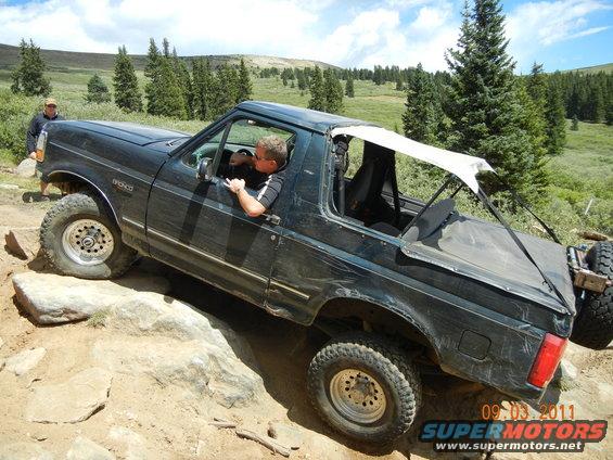 Black 1996 Ford Bronco navigating rocks on an off-road trail with a driver and passenger