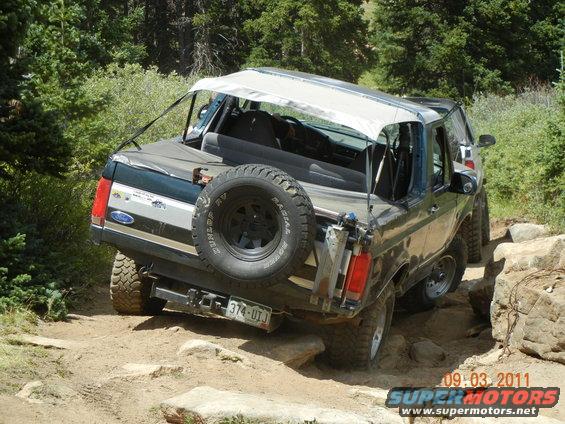 1996 Ford Bronco rear view, dark green with white soft top, on rocky trail