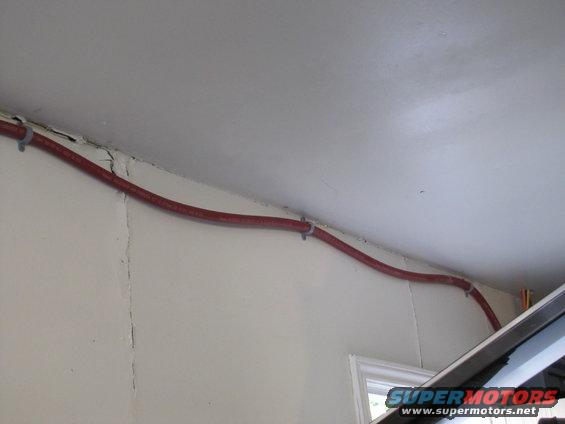 Red conduit secured with zip ties to a white ceiling and wall junction