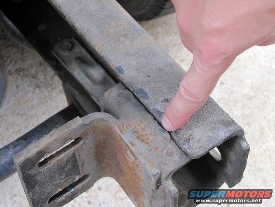 Close-up of a cracked vehicle frame with a finger pointing to the damage