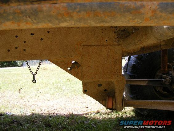 Underside of a rusty vehicle frame with a chain hanging down. Large tire visible on the right
