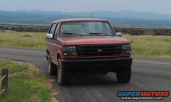 Red 1995 Ford Bronco driving on a road with a mountainous landscape in the background