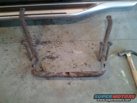 rusted metal step bar with mounting brackets, next to a hammer on concrete floor