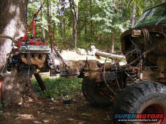 engine and transmission being lifted out of a rusty truck frame with a tree and engine hoist
