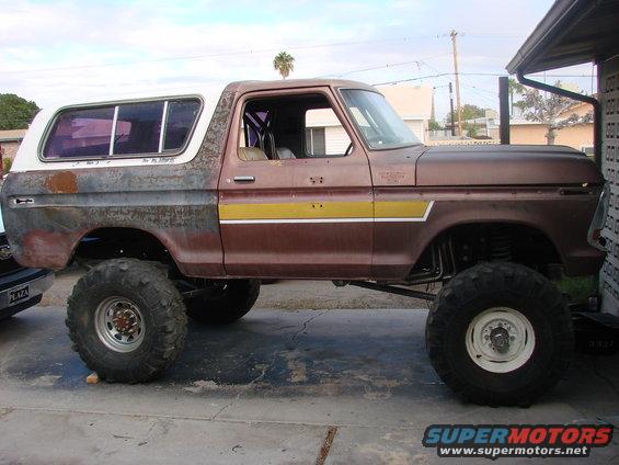 Side view of a lifted 1979 Ford Bronco with a brown body, white top, yellow stripe, and visible roll cage
