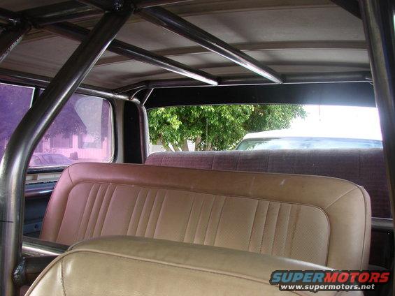 Interior view of a vehicle with a roll cage and tan seats. Another vehicle is visible through the rear window