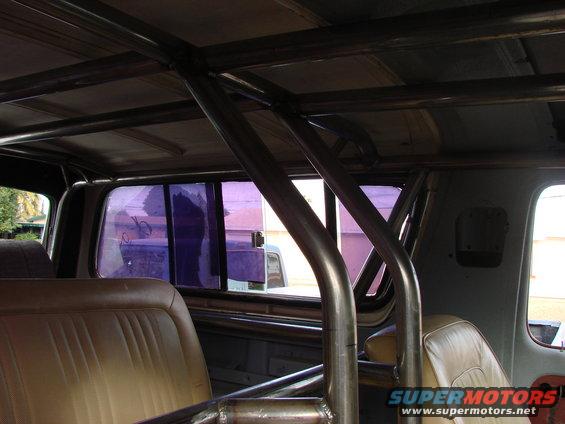 Interior view of a vehicle with a custom metal roll cage and tan seats, showing purple tinted windows