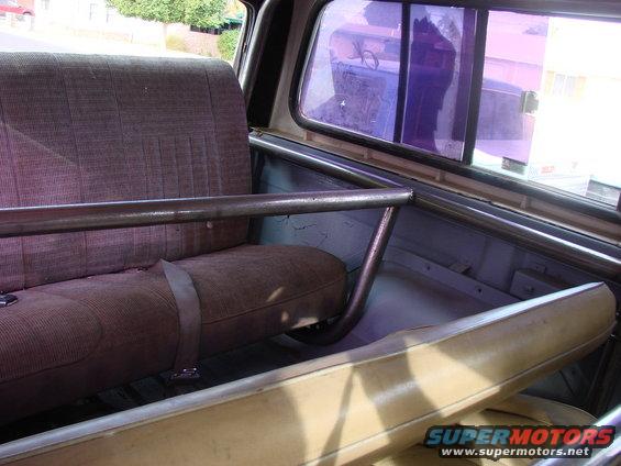 Interior view of a vehicle showing fabric seats and a metal roll cage. A seatbelt is visible