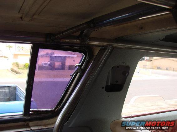 Interior view of a vehicle with a roll cage, looking out the window at a house and a blue pickup truck bed