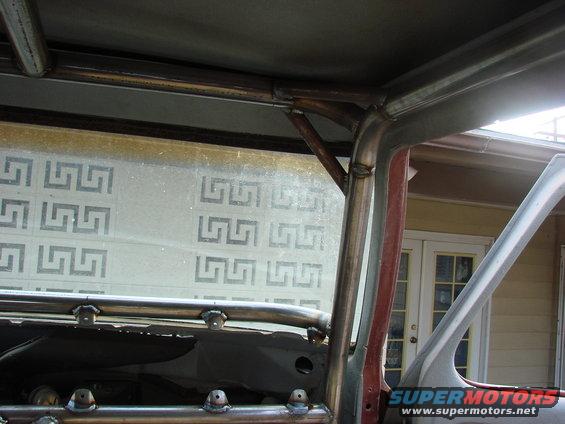 Close-up of metal roll cage tubing welded inside a vehicle. Window has a Greek key pattern