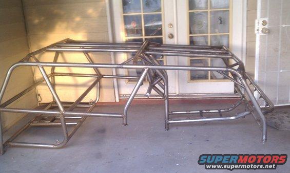 Metal roll cage frame with multiple bars and supports, resting on a concrete surface