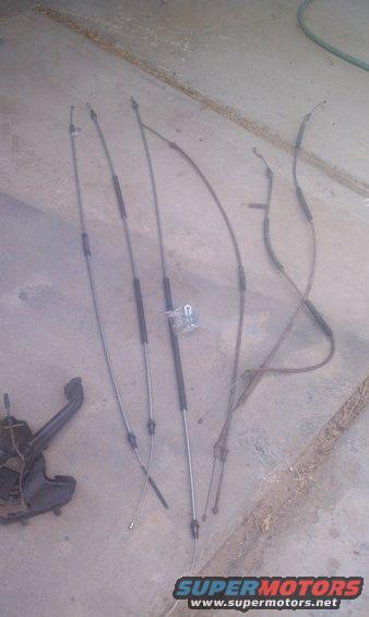 Several parking brake cables and a metal bracket on a concrete surface