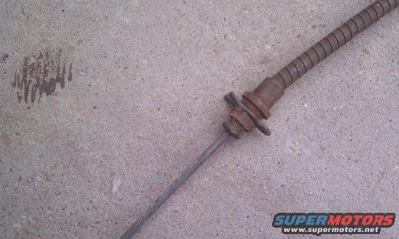 Close-up of a rusty parking brake cable with a coiled metal sheath, lying on a concrete surface