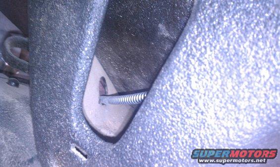Close-up of a parking brake cable with a coiled spring passing through a bracket