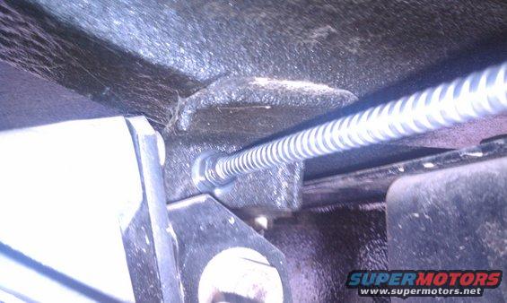Close-up of a coiled parking brake cable attached to a metal bracket under a vehicle