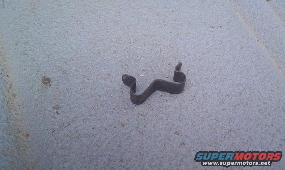 Small, dark, bent metal clip on a textured surface