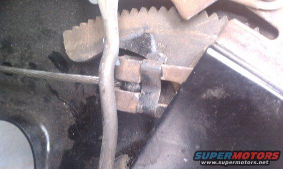 Close-up of a rusty parking brake mechanism with a steel cable and toothed gear