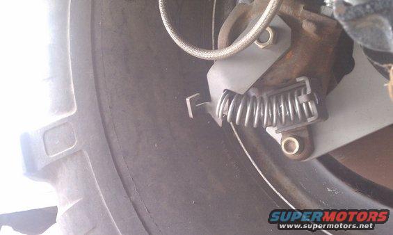 Close-up of a vehicle's parking brake assembly with a spring and metal bracket near a tire