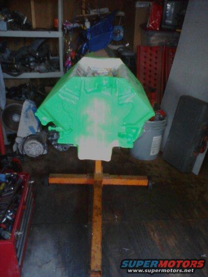 Green engine block on an orange stand in a garage. Tools and shelves in background
