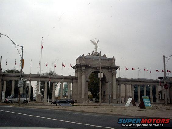 Monument with many Canadian flags and two cars parked in front