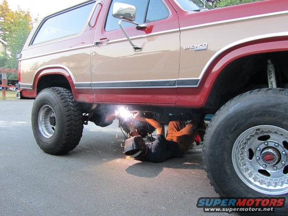 Two-tone red and tan Ford Bronco with a person welding underneath
