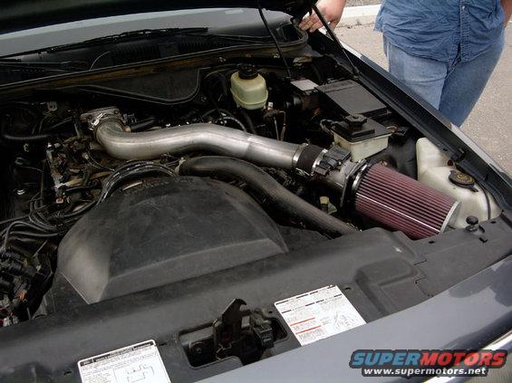 Gray Ford Crown Victoria engine bay with aftermarket air intake. Hood is open, person in blue shirt and jeans visible
